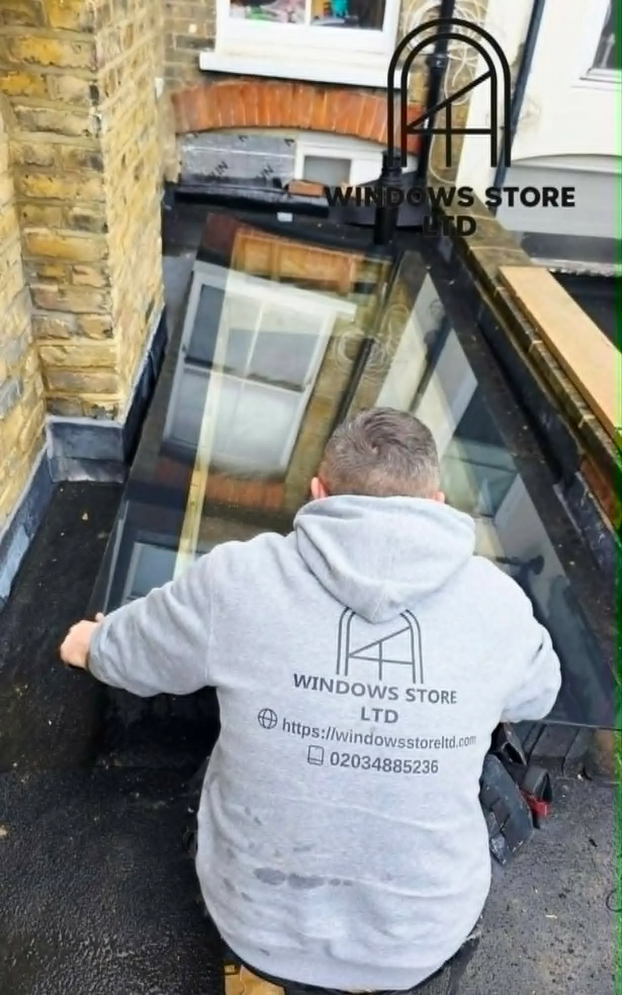 A Windows Store Ltd fitter guiding a large glass rooflight panel into place over a flat roof, London